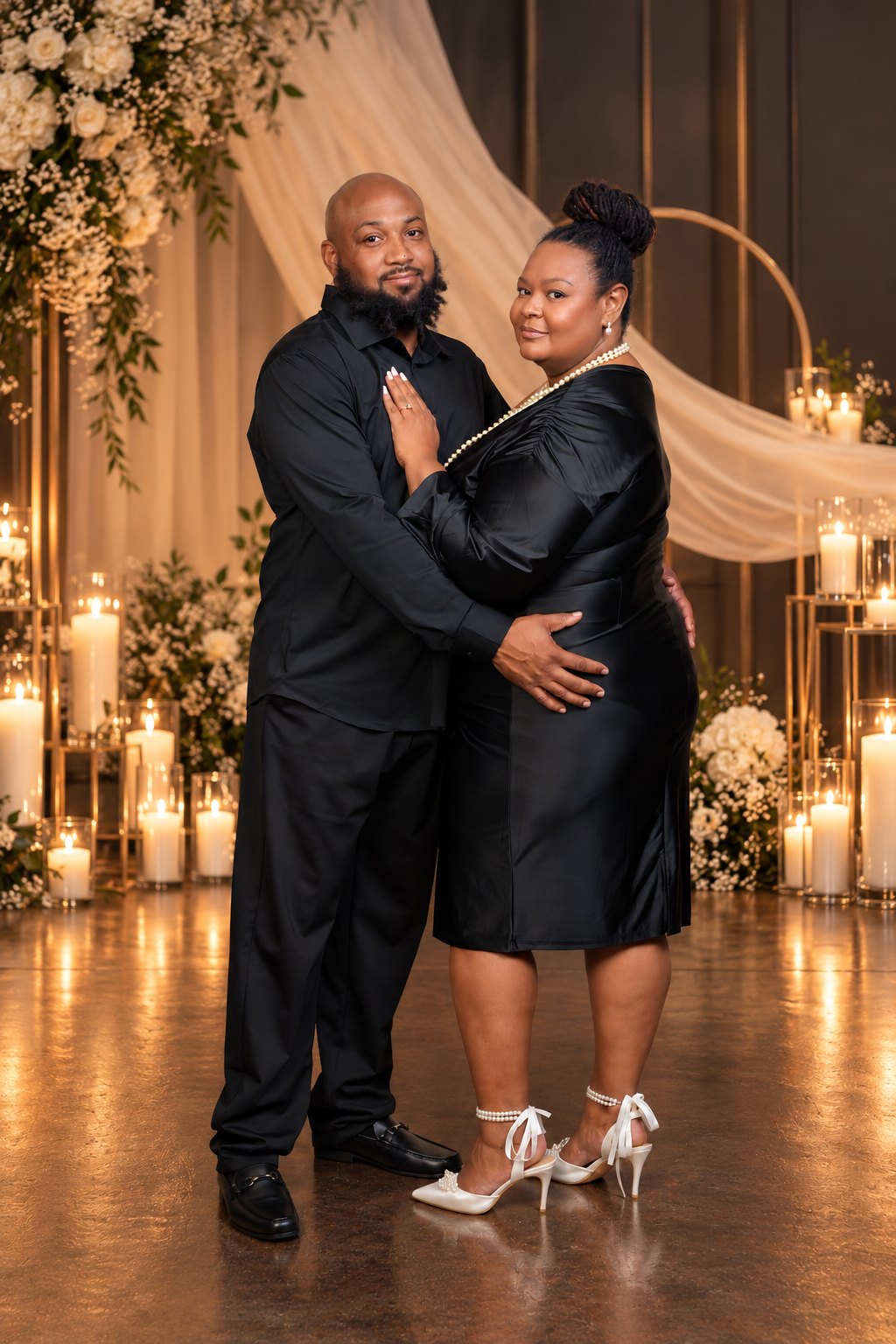 Juliette and Anthony in black, standing before candles, white roses and a gold arch
